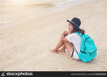 Young woman with backpack sitting on lonely beach and looking into distance.