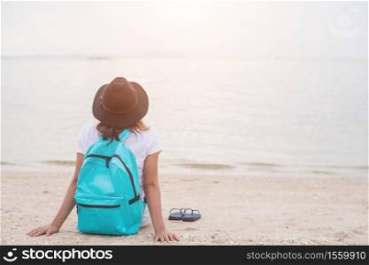 Young woman with backpack sitting on lonely beach and looking into distance.