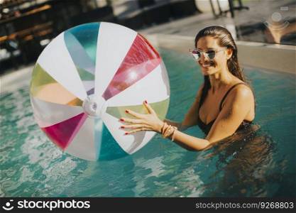 Young woman with ball in the pool at sunny day