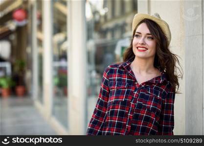 Young woman with beautiful blue eyes wearing plaid shirt and sun hat. Girl smiling in urban background.