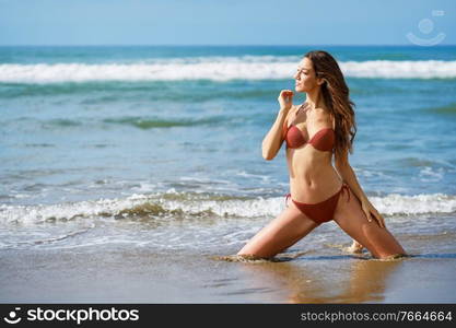 Young woman with beautiful body on her knees on the sand of the beach. Woman with beautiful body on her knees on the sand of the beach