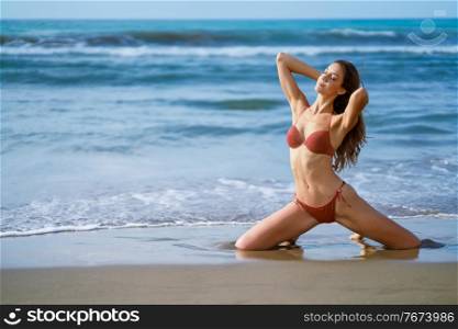 Young woman with beautiful body on her knees on the sand of the beach. Woman with beautiful body on her knees on the sand of the beach