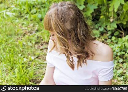 Young woman with blond hair sitting on green grass in summer