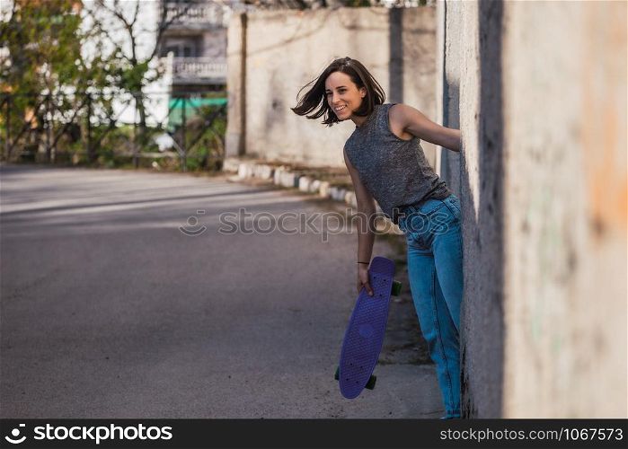 Young woman with blue penny skateboard in casual wearing grabs ancient metal industrial door, freedom concept