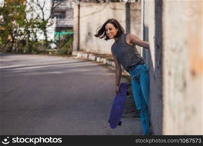 Young woman with blue penny skateboard in casual wearing grabs ancient metal industrial door, freedom concept