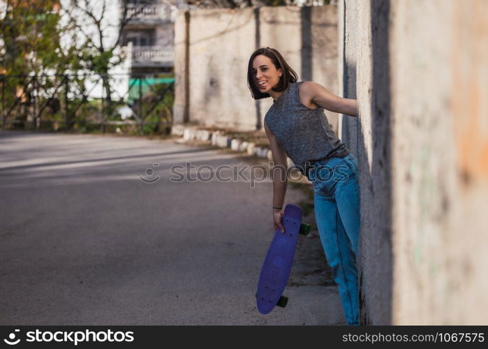 Young woman with blue penny skateboard in casual wearing grabs ancient metal industrial door, freedom concept