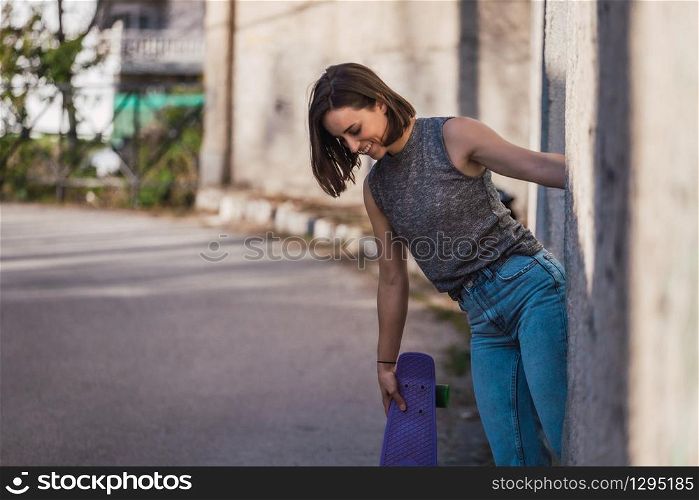 Young woman with blue penny skateboard in casual wearing grabs ancient metal industrial door