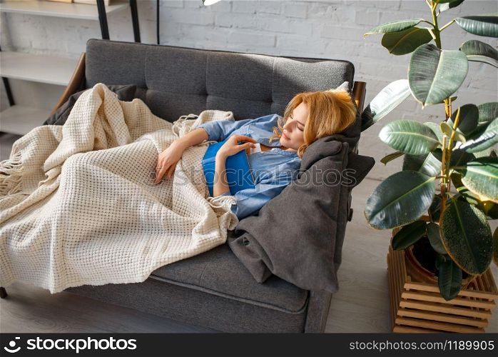 Young woman with book fell asleep under a blanket on cozy black couch, living room in white tones on background. Attractive female person with magazine rest on sofa at home