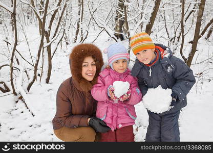 young woman with boy and little girl in winter in wood, children keeps in hands snowballs