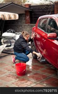 Young woman with bucket and rag washing red car