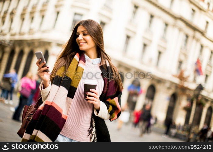 Young woman with cell phone and coffee to go walking on the street