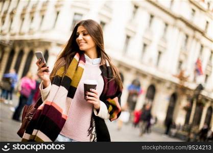 Young woman with cell phone and coffee to go walking on the street