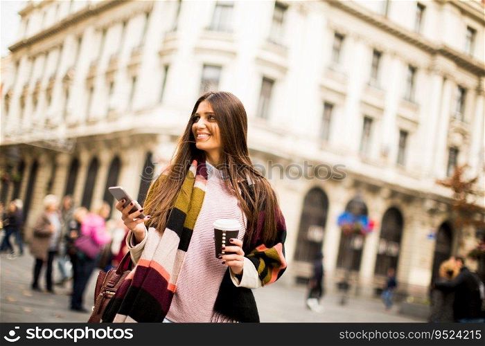 Young woman with cell phone and coffee to go walking on the street