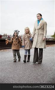 Young woman with children in warm clothing walking together on street