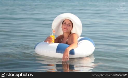 Young woman with cocktail in hand floating on innertube