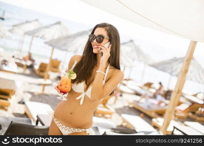 Young woman with coctail spaeking on mobile telephone on the beach