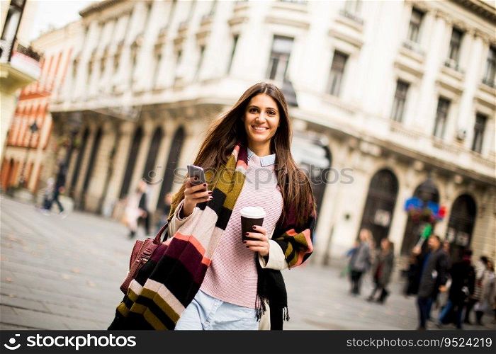 Young woman with  coffee to go and  mobile phone in hand walking down the street