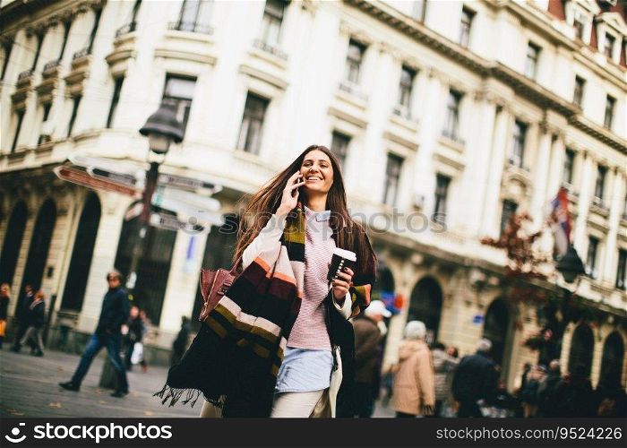 Young woman with coffee to go and mobile phone in hand walking down the street