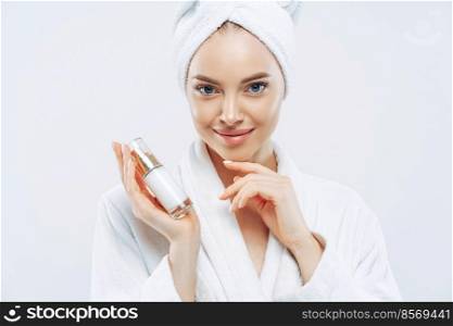 Young woman with confident expression, healthy clean smooth skin, well groomed complexion, holds bottle of lotion or gel, touches jawline, dressed in bath robe. Beauty and cosmetics concept.