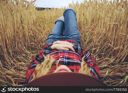 Young woman with country style is resting in a field of wheat
