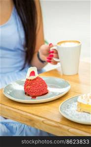 Young woman with cup of coffee and piece of cake sitting at the table in a cafe outdoors. Young woman sitting at the table in cafe