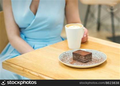 Young woman with cup of coffee and piece of cake sitting at the table in a cafe outdoors. Young woman sitting at the table in cafe