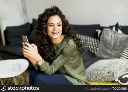 Young woman with curly hair sitting on the sofa in the room and using a mobile phon