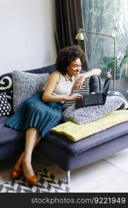 Young woman with curly hair, uses  laptop and sitting on the sofa at home