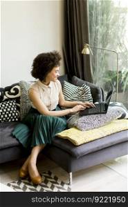 Young woman with curly hair, uses  laptop and sitting on the sofa at home