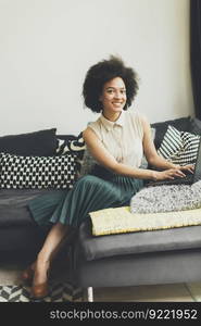 Young woman with curly hair, uses  laptop and sitting on the sofa at home