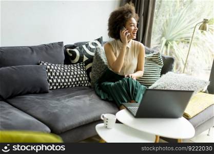 Young woman with curly hair, uses laptop and sitting on the sofa at home