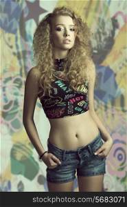 young woman with curly natural hair posing in fashion shoot with trendy top and casual denim short, sensual eyes looking in camera