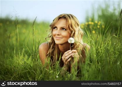 Young woman with dandelion lying on grass