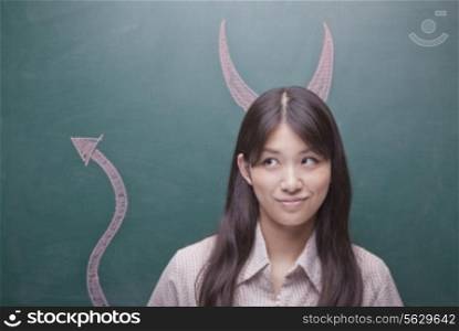 Young woman with devil horns and tail on blackboard