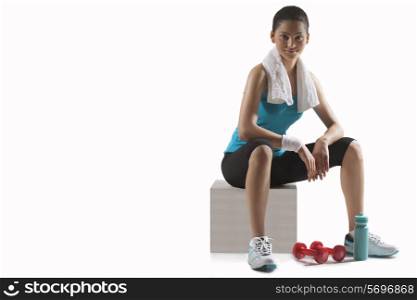 Young woman with dumbbells sitting on stool isolated over white background