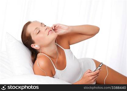 Young woman with ear buds in white holding mp3 player