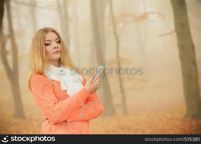 Young woman with earphones and smartphone listening music. Girl in foggy fall autumn park.. Woman with earphones listening music in park.