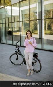 Young woman with ebicycle using on mobile phone outdoor