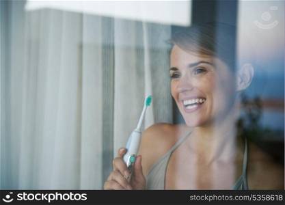 Young woman with electric toothbrush and looking in window