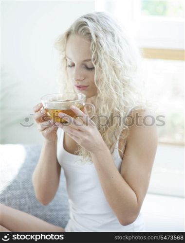 Young woman with eyes closed enjoying herbal tea in house