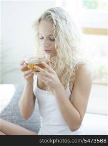 Young woman with eyes closed enjoying herbal tea in house