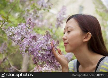 Young woman with eyes closed smelling a flower blossom in the park in springtime