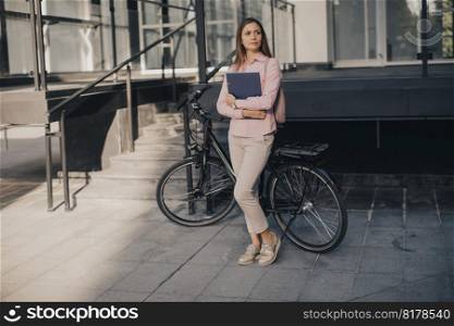 Young woman with files in the  hands standing outdoor in front of electric bike