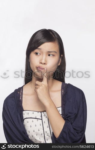Young woman with finger to her mouth contemplating, studio shot