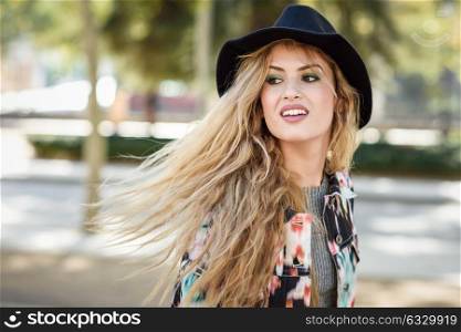 Young woman with flying hair wearing jacket and hat, happy in urban background