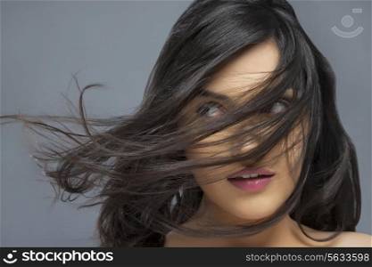 Young woman with hair blowing over face against colored background