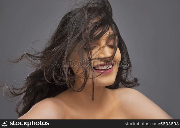 Young woman with hair blowing over face against colored background