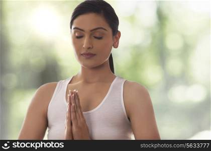 Young woman with hands clasped meditating against glass window