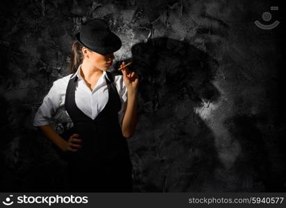 Young woman with hat and cigar on grey wall