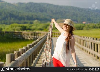 young woman with hat in red pants, white shirt, with a hand in the form of a bouquet, smiling happily on a wooden road .. A glorious spring day ..